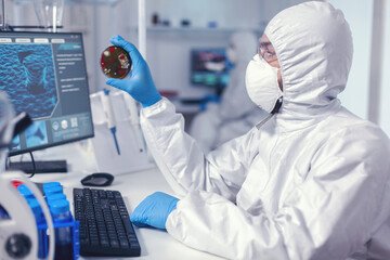 Medicine researcher works on sars-cov-2 on petri dish dressed in coverall. Doctors analysing...