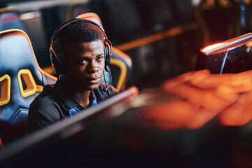 Young african guy, male professional cybersport gamer wearing headphones looking at camera while...