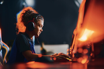 Side view of a young mixed race girl, female cybersport gamer wearing headphones playing online video games, participating in eSport tournament