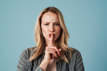 Displeased beautiful girl looking at camera and showing silence gesture