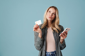 Thinking beautiful blonde girl posing with credit card and mobile phone