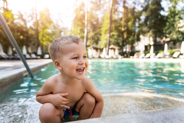 Fototapeta na wymiar Little cute adorable blond playful beautiful caucasian active toodler boy enjoy playing at pool edge at summertime outdoor sea forest resort area. Happy kid friend leisure vacation travel concept