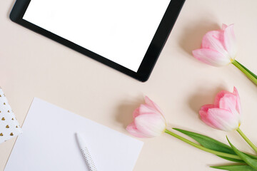 Flat flat top view mock up: digital tablet and pink tulips on beige background. Copy space and flat lay. The concept of the blog for spring, Mother's day, Valentine's day