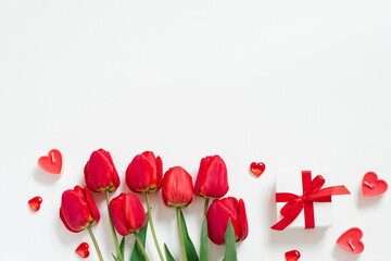 Valentine Day Romantic Background. Red tulips, a gift with a bow, and candle hearts on a white background with copying space. Flat lay