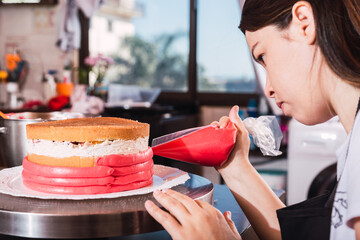Beautiful young girl concentrating and decorating a cake - Young baker in apron works in the kitchen.