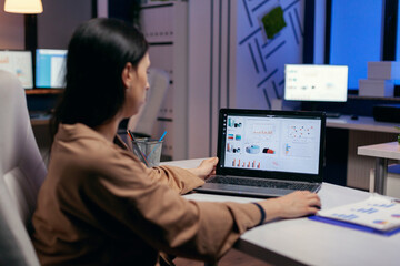 Manager working on financial reports late at night sitting at desk in empty office. Businesswoman looking at statistics on laptpop screen sitting at her workplace doing overtime.