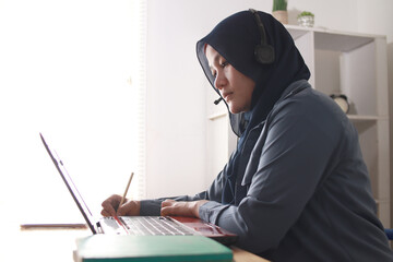 Asian muslim woman having video teleconference on her laptop at home, online learning or working...