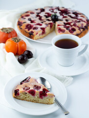 Blurred image of a piece of fruit pie on a white plate in the background a cup of tea, fruit and a pie.