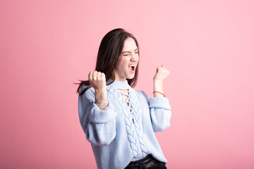 Smiling, happy and winning brunette girl in studio on pink background