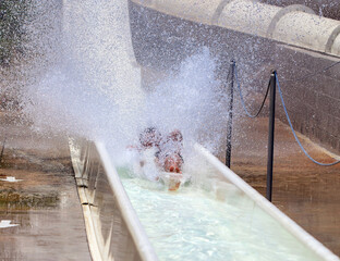 People having fun at waterpark. There are legs of man sliding down slide under water.