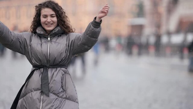 positive woman is walking on city square at winter day, dressed down jacket, laughing happily