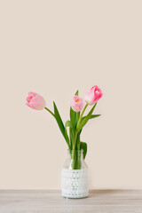 Obraz na płótnie Canvas A bouquet of three pink tulips stands in a glass vase with lace. The concept of the spring festival