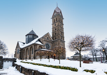 Fototapeta na wymiar Beautiful church in Butgenbach surrounded by a winter landscape with illuminated Christmas lights in the trees around Christmas time. 