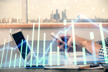 Double exposure of man's hands holding and using a digital device and forex graph drawing. Financial market concept.