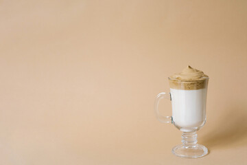 Beautiful dalgon drink coffee with foam in a transparent mug on a beige background with space copying