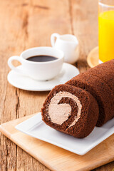 Chocolate cake roll with cup of coffee orange juice and milk on wooden table, Breakfast set concept.