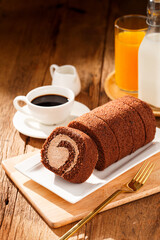 Chocolate cake roll with cup of coffee orange juice and milk on wooden table, Breakfast set concept.