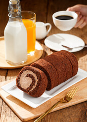 Chocolate cake roll with cup of coffee orange juice and milk on wooden table, Breakfast set concept.