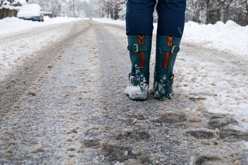 Woman in rubber boots on a snowy and slippery road. Weather and movement