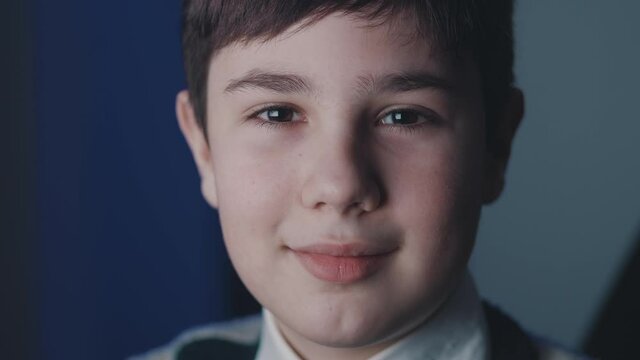 Close-up portrait of cute boy 13 years old looking at camera while sitting at computer laptop at home at nighttime. People, lifestyle and youth concept.
