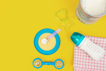 Milk powder for baby in measuring spoon in can and milk bottle on fabric on yellow background