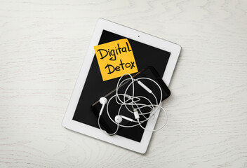 Different gadgets and sticking paper with words DIGITAL DETOX on white wooden background, top view