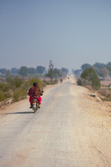 Two villagers on bike in ruler area passing through agricultural field