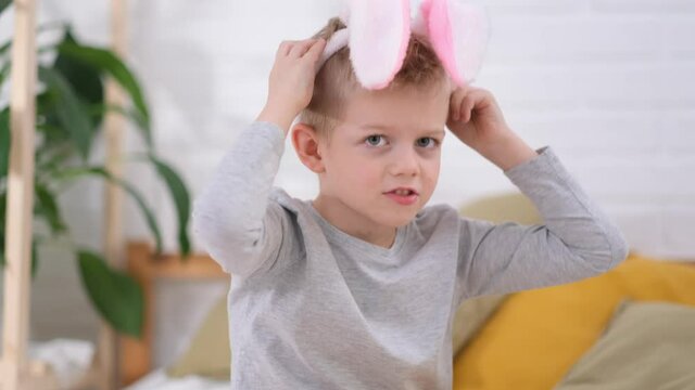 Portrait Easter kid. Boy putting on rabbit bunny ears on head having fun at home. Cheerful smiling child