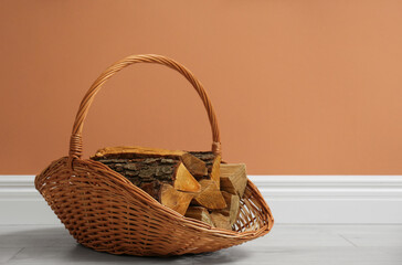 Wicker basket with firewood near brown wall indoors, space for text