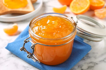 Tasty tangerine jam in glass jar on white marble table