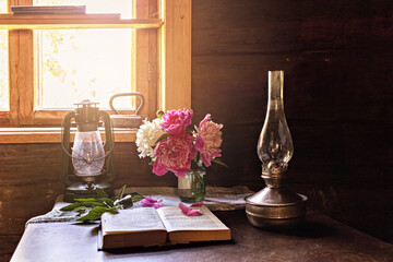 Still life of vintage items and a bouquet of peonies on a table by the window in an old village...