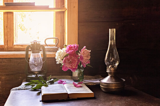 Still life of vintage items and a bouquet of peonies on a table by the window in an old village house.