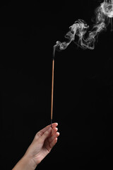 Woman holding smoldering incense stick on black background, closeup