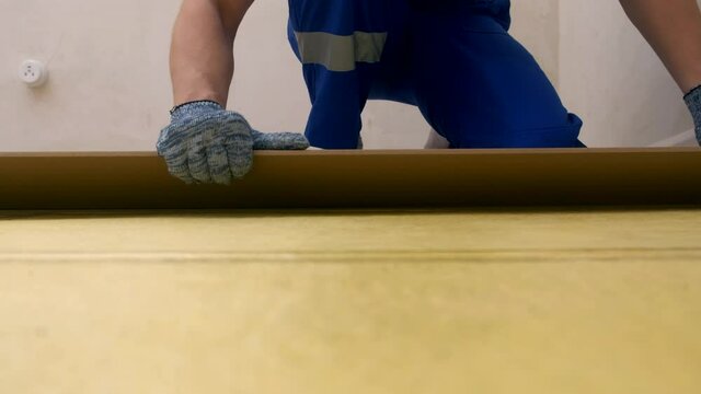 A construction worker in a blue uniform and gloves puts a laminate board on the floor and inserts it into another part