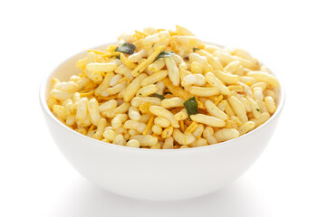 Crunchy Murmura in a white ceramic bowl, made with Puffed Rice and Curry leaves. Pile of Indian spicy snacks (Namkeen), under backlight, side view, against the white background.