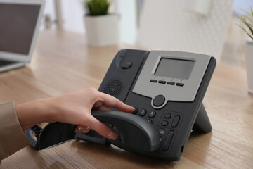 Woman using desktop telephone at wooden table in office, closeup. Hotline service