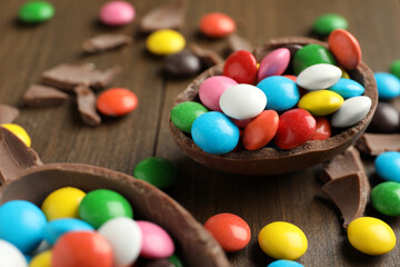 Broken chocolate egg and colorful candies on wooden table, closeup