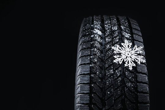 Winter tire with decorative snowflake on black background, closeup. Space for text