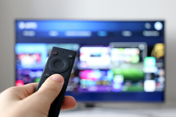 Male hand with remote controller on smart TV screen background. Person choosing streaming services,...
