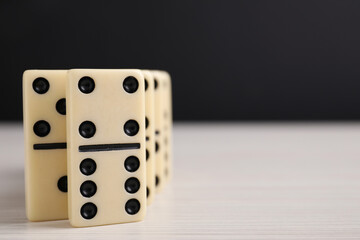 Domino tiles on wooden table against black background, closeup. Space for text