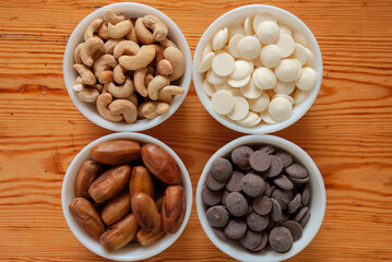 Food ingredients in white bowls. Cashews, dates, white and milk chocolate drops in white small bowls.