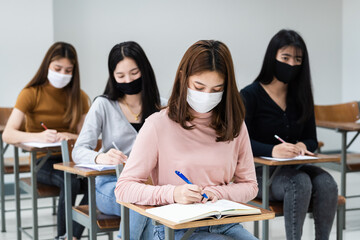 Female teenager college students wears face mask and keep distance while studying in classroom and college campus to prevent COVID-19 pandemic