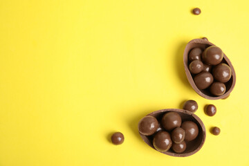 Halves of tasty chocolate egg with candies on yellow background, flat lay. Space for text