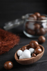 Half of tasty chocolate egg with candies on black wooden table, space for text