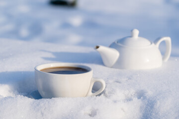 Obraz na płótnie Canvas White cup of hot tea and teapot on a bed of snow and white background, close up