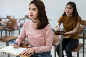 Selective focus of the teen college students sitting on lecture chair in classroom write on examination paper answer sheet in doing the final examination test. Female students in the student uniform.