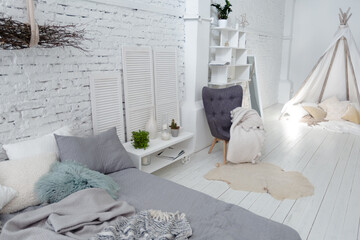 Spacious stylish modern trendy loft apartment in white and light colors. brick wall, wood floor, shelving, pallet bed and teepee-shaped children's house. everything is white with gray tints.