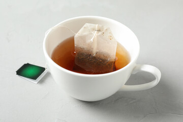 Tea bag in cup of hot water on light grey table