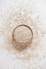 Dry oatmeal in a wooden bowl and is randomly scattered on a white background. Top view. Copy, empty space for text
