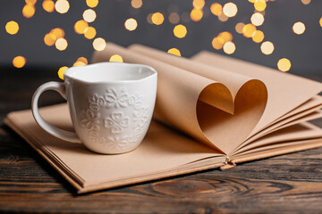 Heart made from book sheets with a cup in lights, love and valentine concept on a wooden table